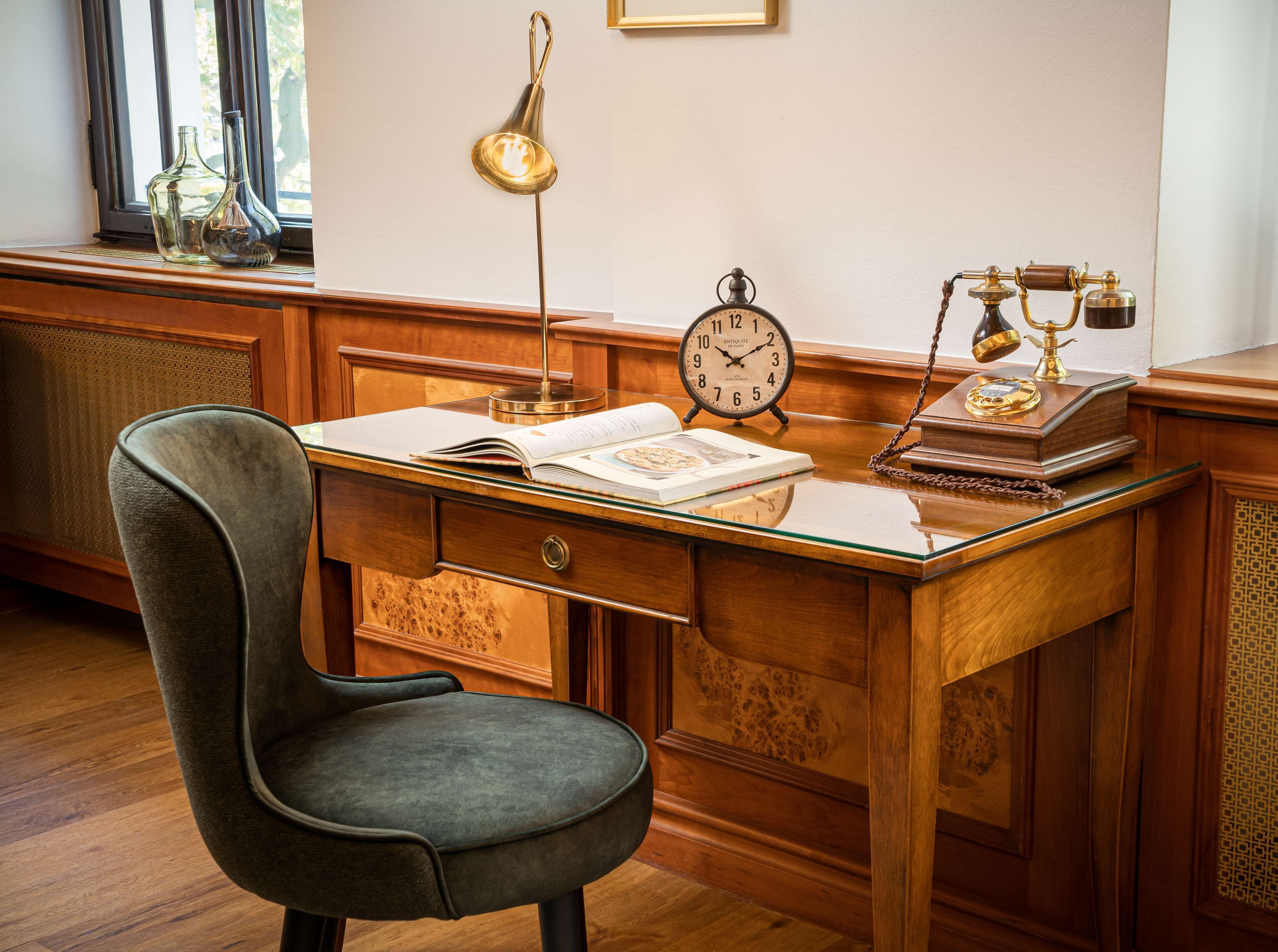 A wooden desk with a vintage clock, a lamp, and a book.