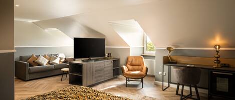 A modern loft bedroom with a large bed, a sofa, a desk, and a TV.