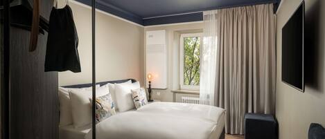 Una habitación de hotel con cama, televisión, ventana con cortinas y radiador.