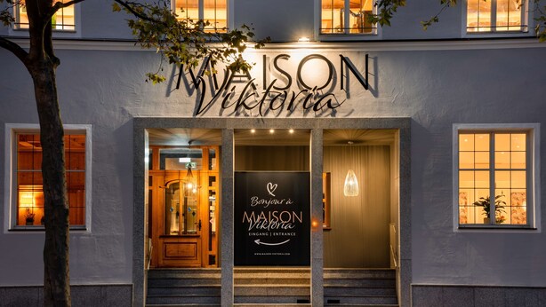 Entrada de un hotel con un cartel que dice "MAISON Viktoria EINGANG | ENTRANCE" y una dirección web.
