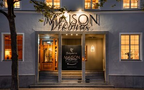 Ein Hotel Eingang mit einem Schild, auf dem steht: MAISON Viktoria EINGANG | ENTRANCE, und einer Website-Adresse.