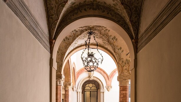 A corridor with ornate arches and a chandelier. - Rolandino Apartment by Wonderful Italy (Bologna)