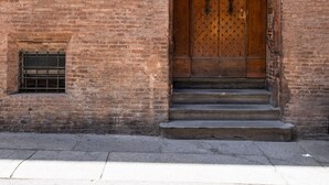 A brick building with a large wooden double door, arched windows, and a small window with a metal grill. - Rolandino Apartment by Wonderful Italy (Bologna)