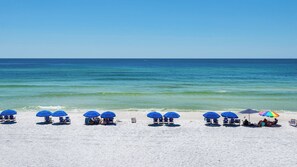 A beach with rows of blue umbrellas and beach chairs, a clear blue sky, and calm ocean waters. - Pool Views & Minutes to Deeded Beach Access + Free Attraction Tickets! (Santa Rosa Beach)