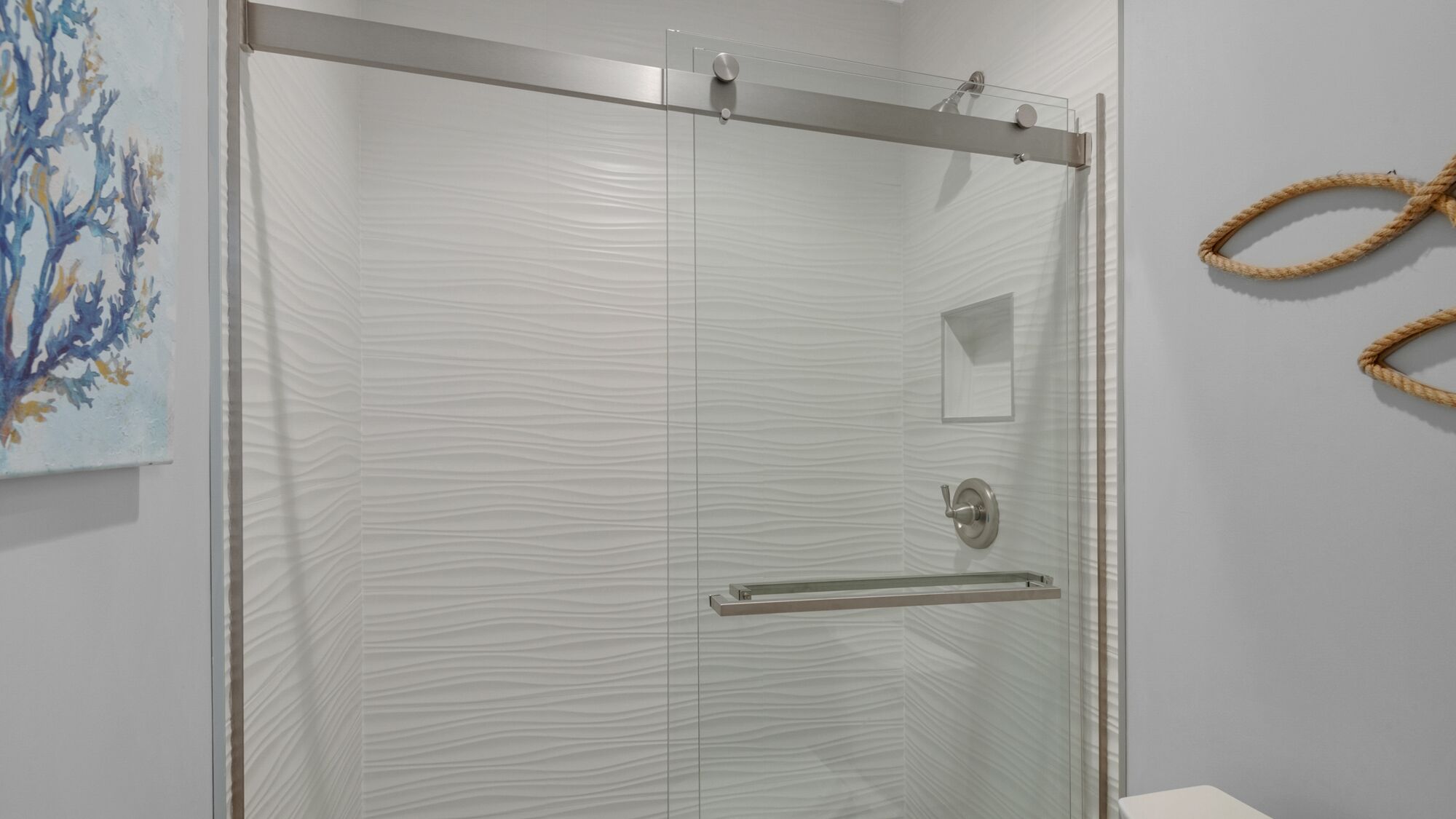 A modern bathroom with a glass shower enclosure, a towel rack, and a painting on the wall.