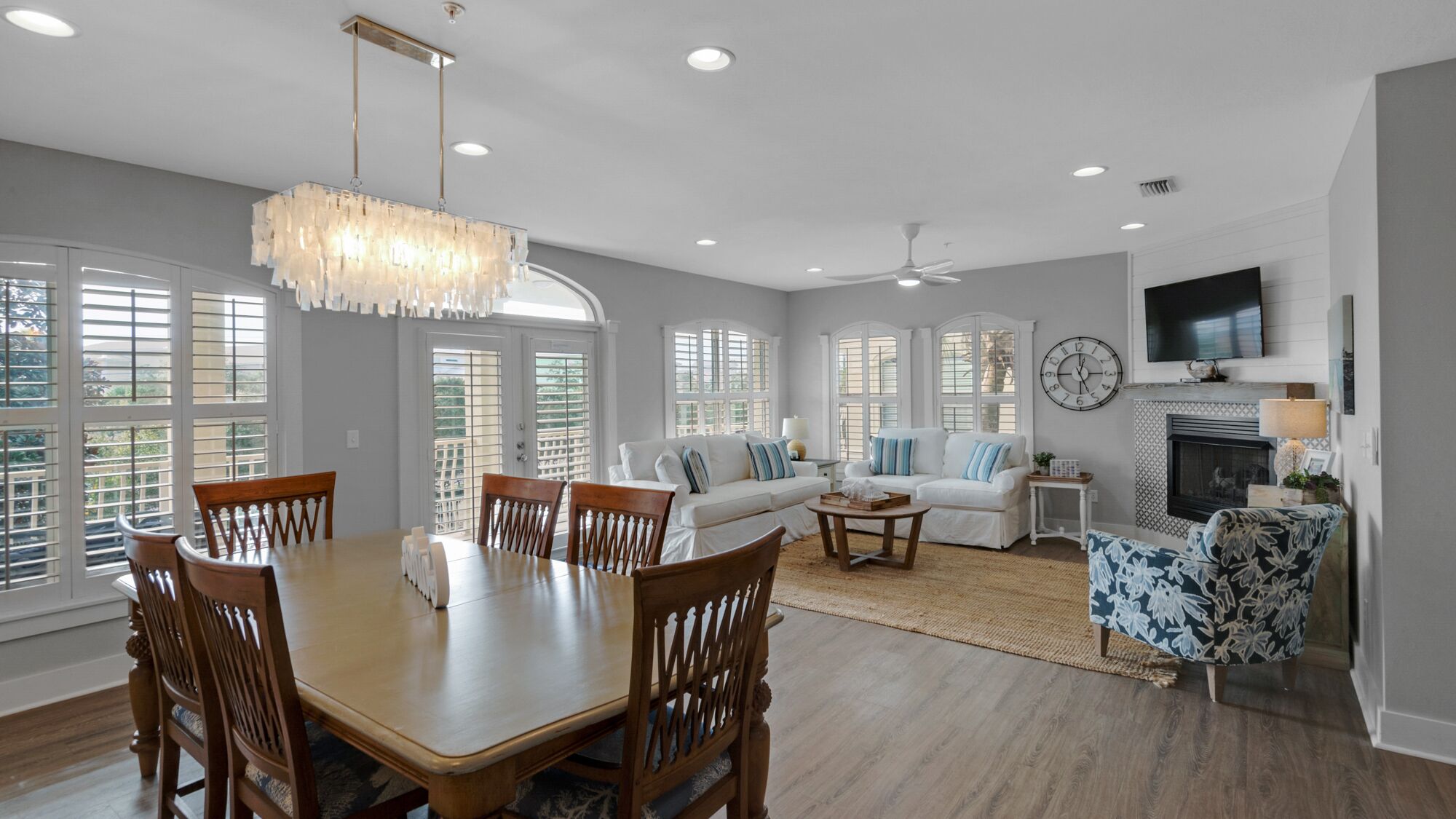 A spacious living room with a dining area, large windows, a fireplace, and a ceiling fan.