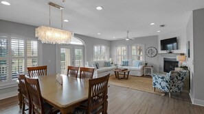 A spacious living room with a dining area, large windows, a fireplace, and a ceiling fan.