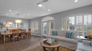 A spacious living room with a dining area, large windows, and a ceiling fan.