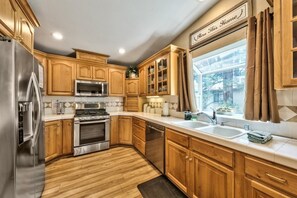 A kitchen with wooden cabinets, stainless steel appliances, and a window with curtains.