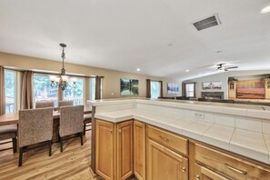 A kitchen with a dining area, wooden cabinets, a large island, and a view of the outdoors.