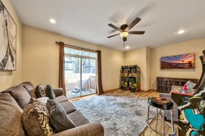 A living room with a sofa, a ceiling fan, a large window, and a painting on the wall.
