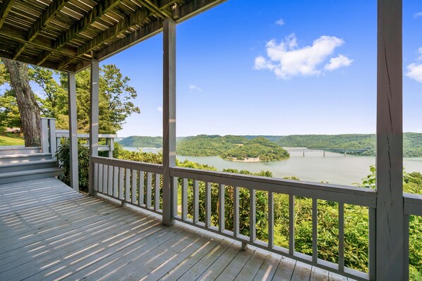 A wooden deck with a railing overlooking a river and forested hills.