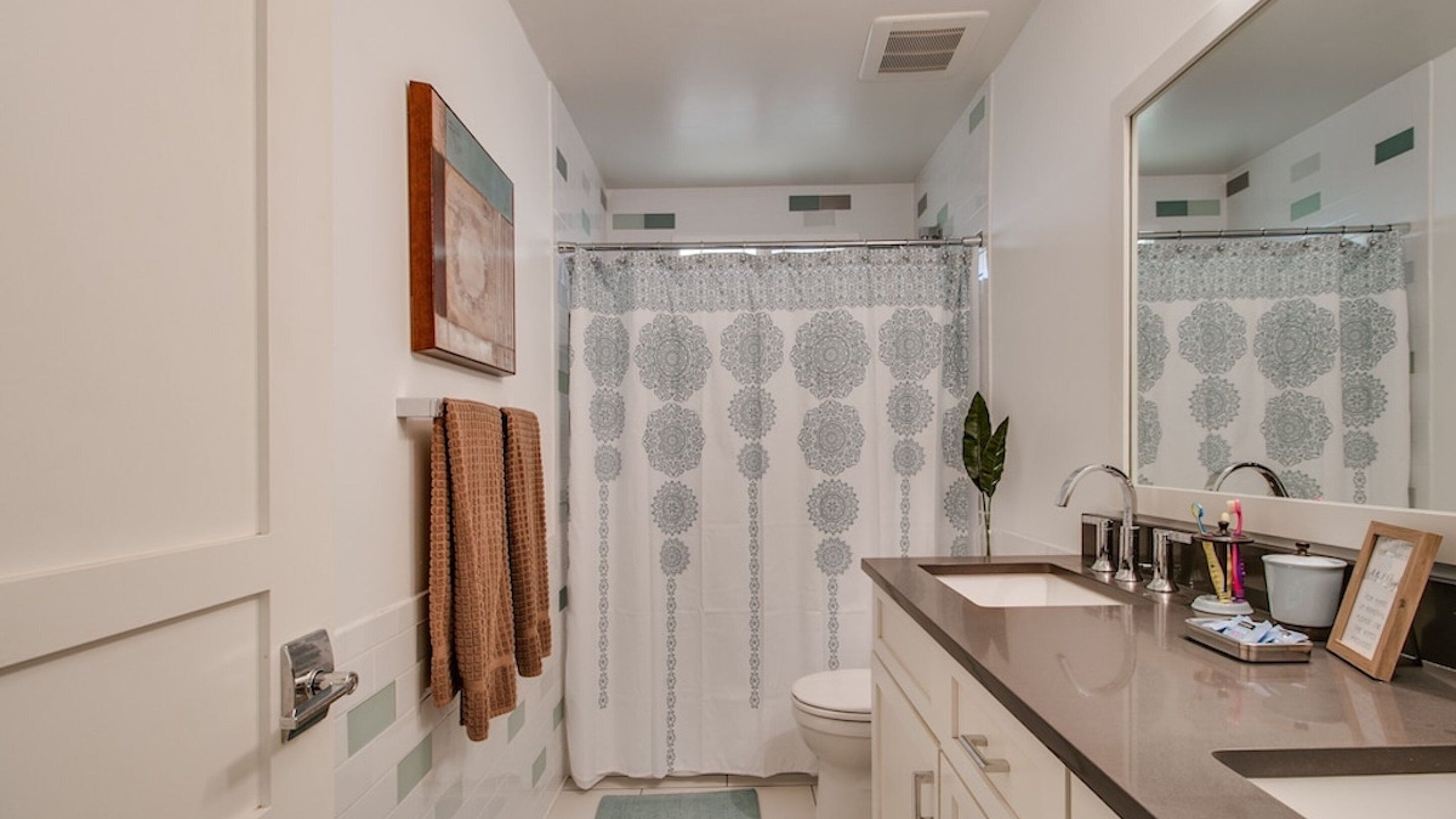 A bathroom with a shower curtain, toilet, sink, and a mirror.