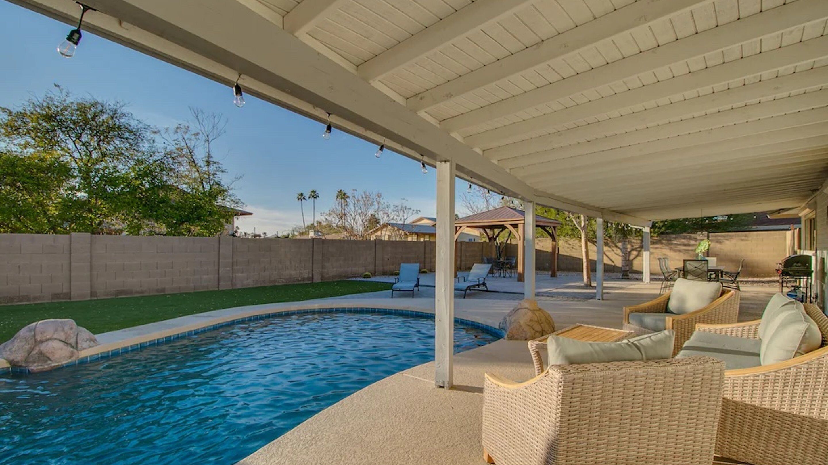 A covered outdoor swimming pool area with lounge chairs and a pergola.