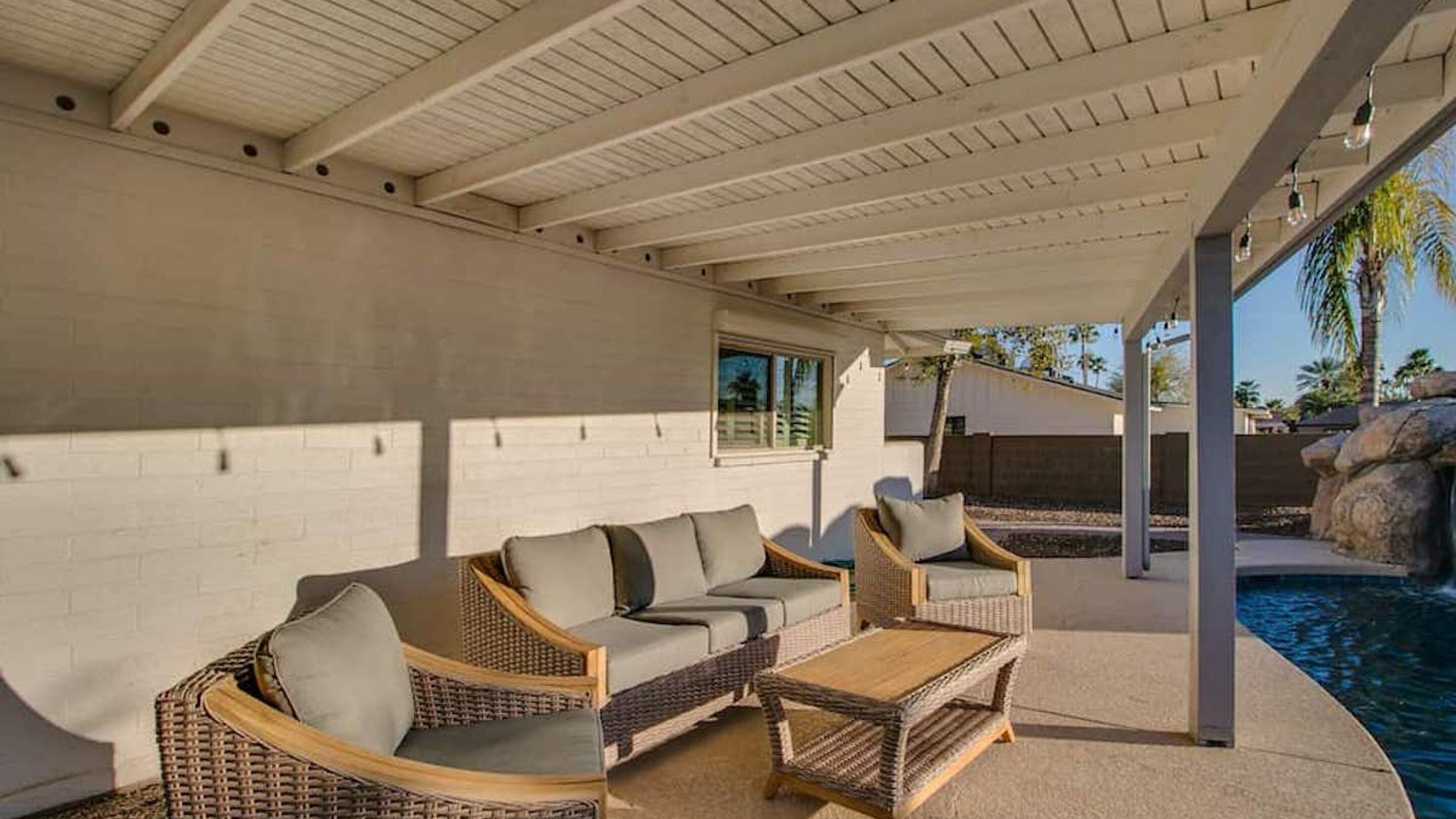 A covered outdoor seating area with wicker furniture and a pool.