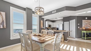 Una cocina moderna con armarios blancos, una isla central y un comedor con mesa y sillas de madera.