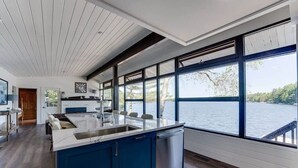Une cuisine moderne dotée d’un grand îlot central, de planchers en bois et offrant une vue sur un lac grâce à de grandes fenêtres.