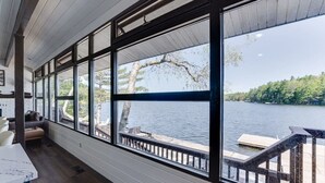 Une pièce dotée de grandes fenêtres donnant sur un lac, d’un plancher en bois et offrant une vue sur un quai.