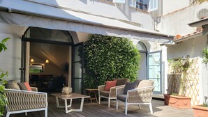 Patio esterno con pavimento in legno, mobili bianchi e parete verde.