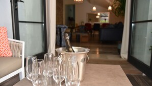 Un tavolo con una bottiglia di champagne e diversi bicchieri, un divano con un cuscino decorato, e vista su una zona giorno con un divano e un tavolo da pranzo.