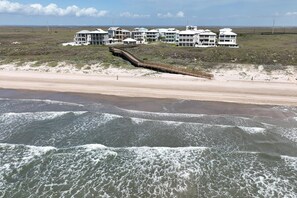 Una propiedad frente a la playa con varios edificios blancos, un paseo marítimo de madera y una playa arenosa.