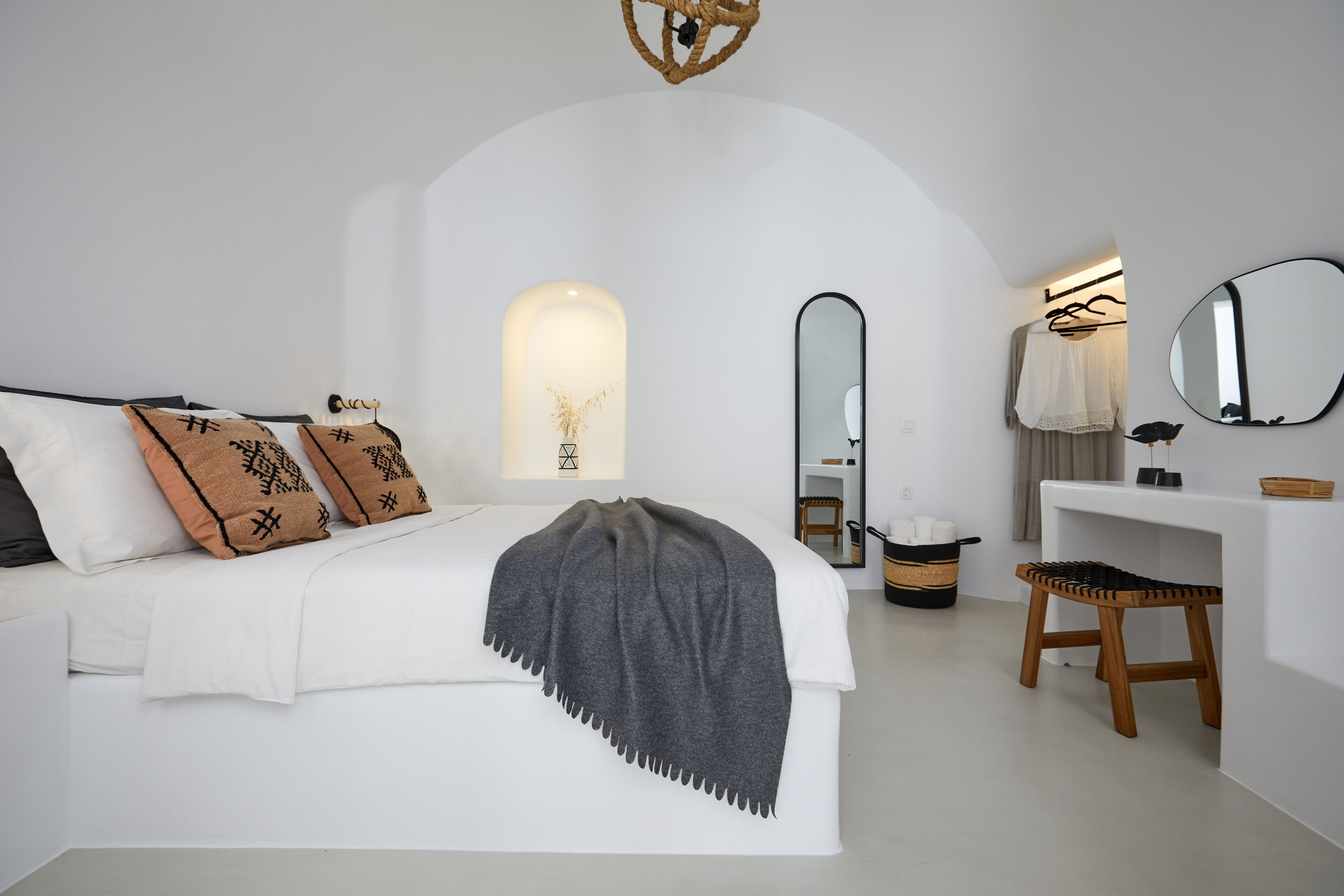 A bedroom with a bed, bedside table, mirror, and a small stool.