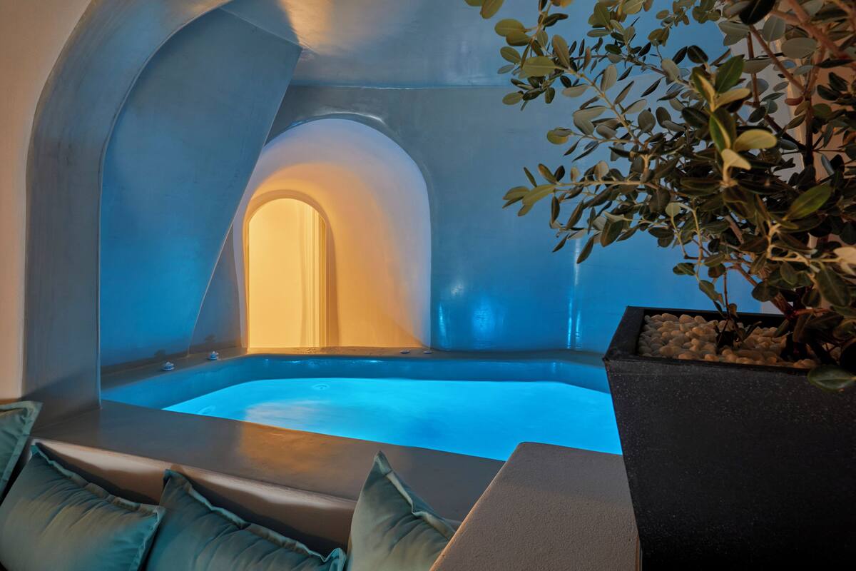 A modern spa room with a hot tub, seating area, and a potted plant.