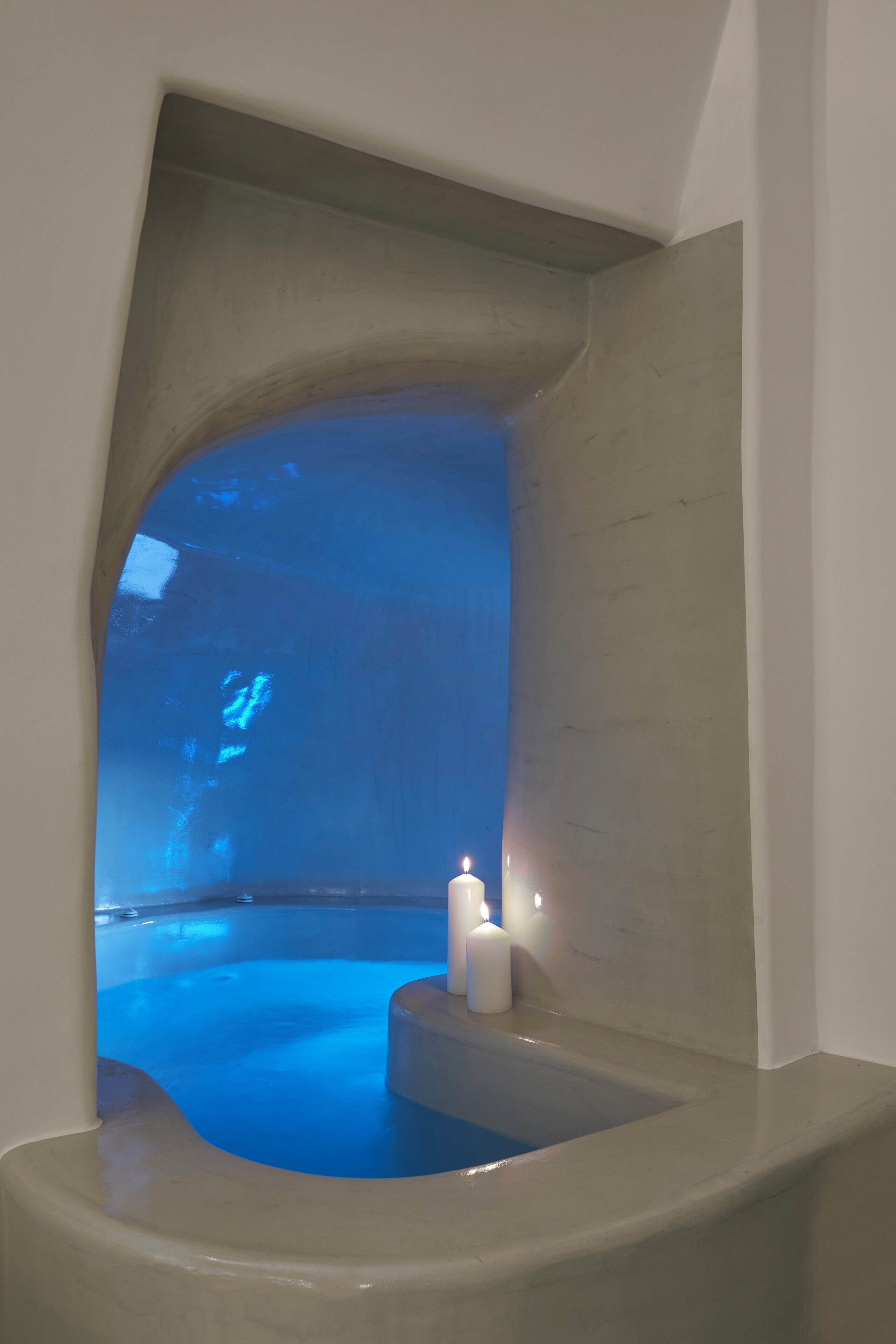 A spa area with a bathtub, candles, and a view of a blue-lit space.