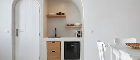 A compact kitchen with a white door, wooden drawers, a black refrigerator, and a small shelf with kitchenware.