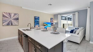 Eine moderne Küche mit einer zentralen Kochinsel, eingebauten Schränken und einem Essbereich mit einem weißen Sofa und einem Fernseher.