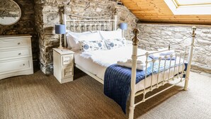 Une chambre avec un mur en pierre, un plafond en bois, un lit avec un cadre en métal, une table de chevet et une lampe.