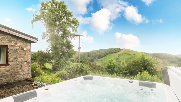 Un bain à remous avec un bâtiment en pierre et une vue sur des collines verdoyantes.