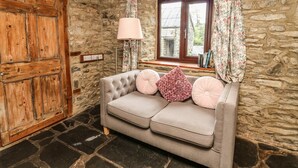 Une pièce chaleureuse avec un mur en pierre, une porte en bois, un canapé confortable, une lampe et une fenêtre avec des rideaux.