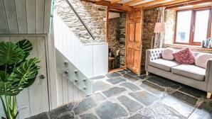 Un intérieur chaleureux avec un sol en pierre, un escalier en bois, un coin salon confortable et un mur en pierre.
