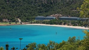 A coastal hotel with multiple buildings, a beach, and a forested hillside. - Frangipani Lodge 104, Frangipani Lodge 104 (Hamilton Island)