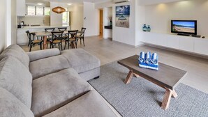 A modern living room with a grey sectional sofa, a wooden coffee table, and a dining area with a table and chairs. - Frangipani Lodge 104, Frangipani Lodge 104 (Hamilton Island)