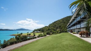 A hotel with a view of a lake and mountains, featuring a well-maintained lawn and a pathway leading to the building. - Frangipani Lodge 104, Frangipani Lodge 104 (Hamilton Island)