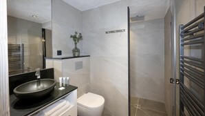 Une salle de bain moderne avec un grand miroir, un plan de toilette noir, des toilettes blanches et une douche à l’italienne en verre.