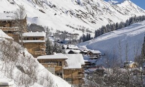 A snow-covered mountain village with wooden buildings, some with balconies, and a clear sky.