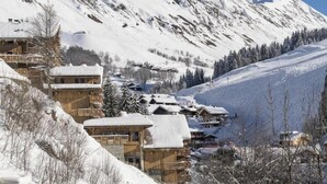 A snow-covered mountain village with wooden buildings, including a chalet and a lodge, surrounded by snow-covered trees and a clear sky. - Wifi, 100m from resort center, view mountain, fitness, swimming pool, sauna, hammam, balcony, tv (Le Grand-Bornand)