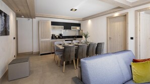 A modern kitchen with a dining area, wooden ceiling beams, and a grey sofa with a yellow pillow. - Wifi, 100m from resort center, view mountain, fitness, swimming pool, sauna, hammam, balcony, tv (Le Grand-Bornand)
