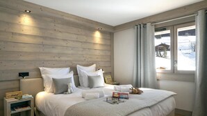 A bedroom with a wooden headboard, a large bed with white bedding, a nightstand with a book and a lamp, and a window with curtains. - Wifi, 100m from resort center, view mountain, fitness, swimming pool, sauna, hammam, balcony, tv (Le Grand-Bornand)