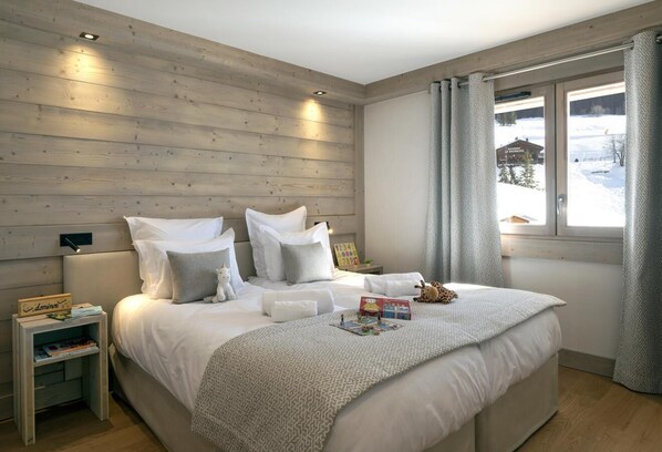 A bedroom with a wooden headboard, a large bed with white bedding, a nightstand with a book and a lamp, and a window with curtains.
