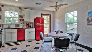 A kitchen with white cabinets, a red refrigerator, and a hexagonal tile floor. There is a dining area with a round table and chairs. - Pancho and Lefty's - Happy Days Escape. 50's Themed getaway! (Wimberley)