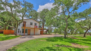 A two-story house with a balcony, surrounded by trees and a grassy lawn. - Pancho and Lefty's - Happy Days Escape. 50's Themed getaway! (Wimberley)