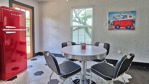 A room with a red Galanz refrigerator, a round table with chairs, a ceiling fan, and a beach van painting on the wall. - Pancho and Lefty's - Happy Days Escape. 50's Themed getaway! (Wimberley)