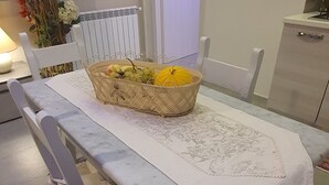 A dining area with a table set for two, a basket of fruit, and a white chair with a floral cushion. - Rosa Apartament (Palermo)