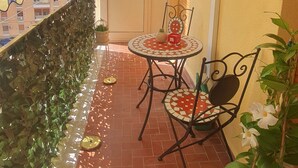 A balcony with a tiled floor, a small table with chairs, hanging plants, and a view of buildings in the background. - Rosa Apartament (Palermo)