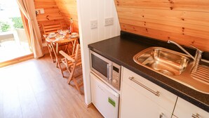 Eine kleine Küche mit Holzwänden, einem Edelstahlspülbecken und einem Essbereich mit Tisch und Stühlen.