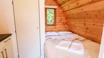 Un dormitorio acogedor con techo de madera, cama con ropa de cama blanca y ventana con vista a la vegetación.